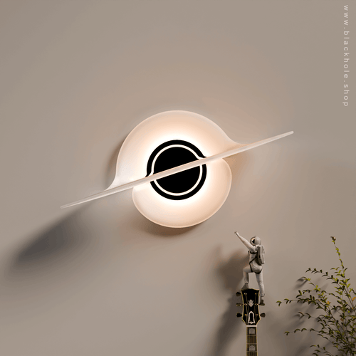 A Black Hole shaped wall lamp mounted on a wall & emitting warm white light.